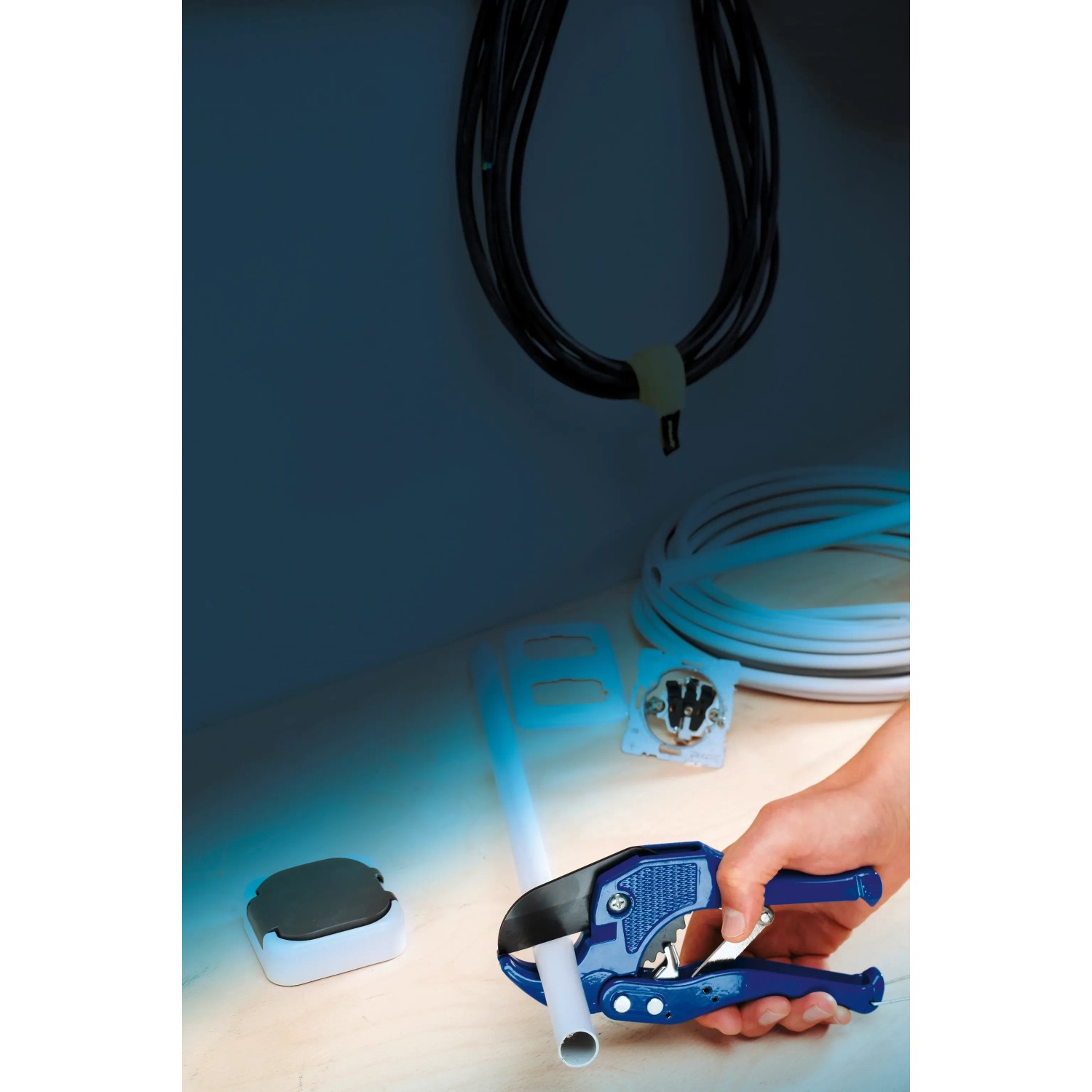 Obcinak do rur LUX PVC 42 mm Classic przecina rurę. Narzędzie z niebieskimi uchwytami.