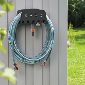 Uchwyt na wąż Gardena z nawiniętym wężem ogrodowym i końcówkami do podlewania.