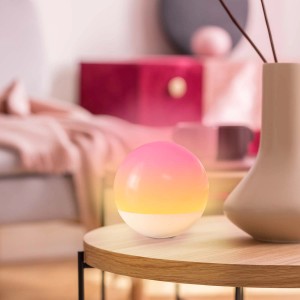 Dekoracyjna lampa stołowa w kształcie kuli z gradientem kolorów od żółtego do różowego.