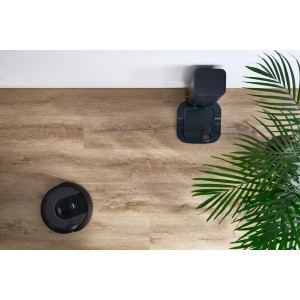 Robot odkurzający ze stacją ładującą na jasnej podłodze winylowej obok rośliny doniczkowej.