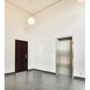 Obszar wejściowy z ciemnymi stalowymi drzwiami, windą i oświetleniem.