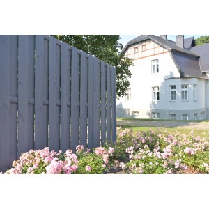 Szare drewniane ogrodzenie w ogrodzie z rabatą kwiatową przed domem.