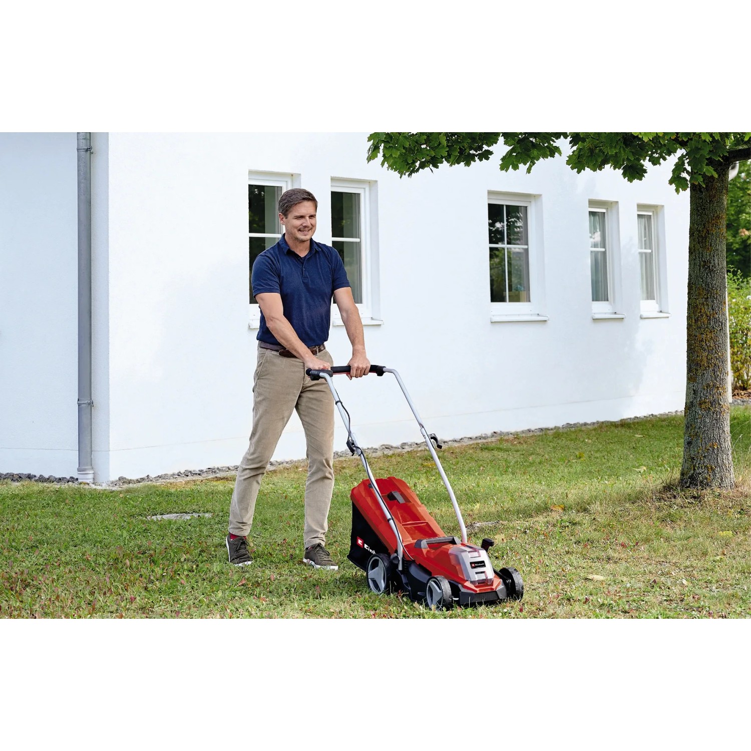 Akumulatorowa kosiarka Einhell Power X-Change GE-CM 18/33 Li z akumulatorem w użyciu na trawniku przed domem.