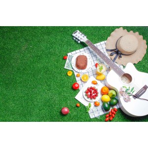 Zielona sztuczna trawa z kocem piknikowym, gitarą, kapeluszem, ciastem i owocami.