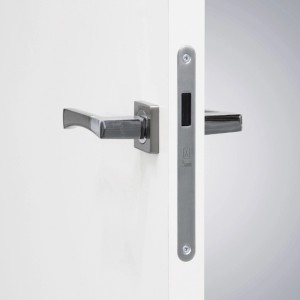 Białe drzwi wewnętrzne z srebrną klamką i zamkiem.