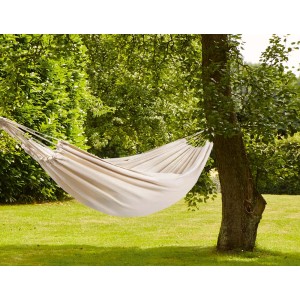 Beżowy hamak z kategorii huśtawek ogrodowych między dwoma drzewami w ogrodzie.