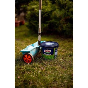 Wiadro nawozu do trawników Substral obok rozsiewacza na trawniku. Nawóz do trawników.