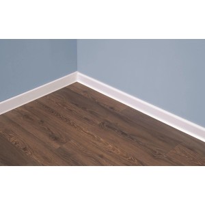 Biała listwa przypodłogowa t.b.t. na ścianie i ciemnej drewnianej podłodze.