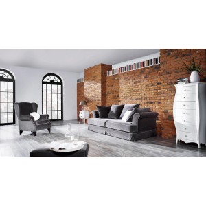 Salon z szarą sofą, fotelem i białą komodą na tle ceglanej ściany.