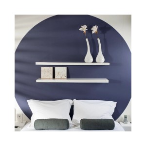 Dwie białe półki ścienne 120 cm nad łóżkiem z dekoracją. Półki do aranżacji salonu.