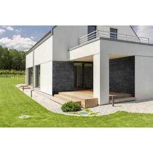 Fasada domu z ciemnymi kamieniami dekoracyjnymi t.b.t. i drewnianym tarasem w ogrodzie.