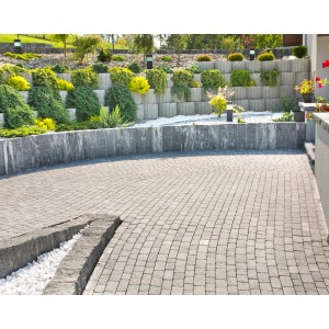 Szara kostka brukowa i szary kamienny mur z roślinami w ogrodzie.