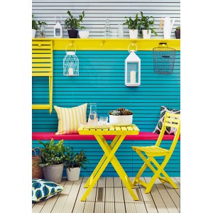 Żółty stół i krzesło na tle niebieskiej ściany z elementami dekoracyjnymi. Farba do użytku zewnętrznego.