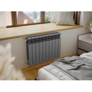 Szary grzejnik t.b.t. pod parapetem w sypialni.