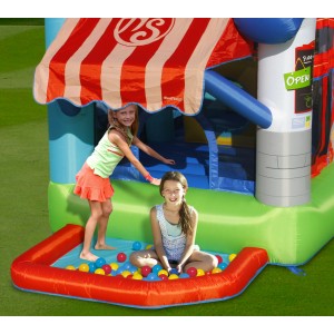 Kolorowy dmuchany zamek t.b.t. z basenem z piłeczkami i dwójką dzieci bawiących się w ogrodzie.