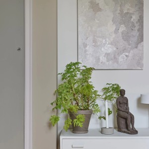 Dekoracyjna scena z farbami do ścian, rośliną, rzeźbą i abstrakcyjnym obrazem.