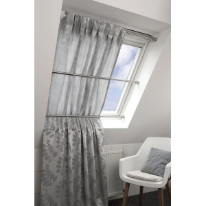 Szara zasłona z motywem liści na srebrnym karniszu t.b.t. przed oknem dachowym.
