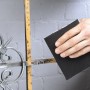 Ręka szlifuje metalową kratę papierem ściernym do metalu LUX K60. Materiał ścierny do średnich prac.