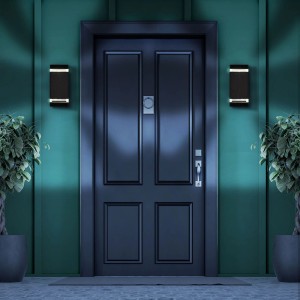 Nowoczesny, czarny kinkiet zewnętrzny t.b.t. zamontowany po bokach drzwi wejściowych.