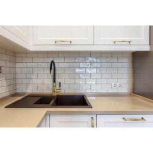 Zlew kuchenny z jednouchwytową baterią t.b.t. w kolorze złotym i czarnym na tle białych szafek kuchennych.