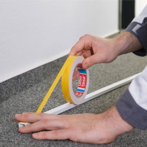 Nakładanie dwustronnej taśmy klejącej na białą listwę.