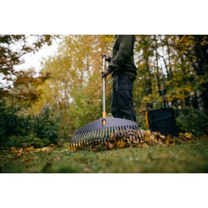 Fiskars Ergonomic Grabie do liści L w użyciu: Osoba grabi liście w ogrodzie szerokimi grabiami.