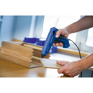 Niebieski pistolet do kleju na gorąco klei elementy drewniane.