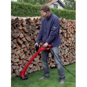 Mężczyzna używa czerwonej elektrycznej kosy t.b.t. do przycinania trawnika w ogrodzie.