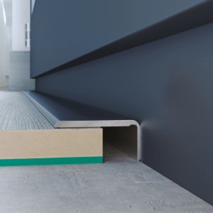 Zbliżenie srebrnej listwy przypodłogowej t.b.t. na szarej ścianie.