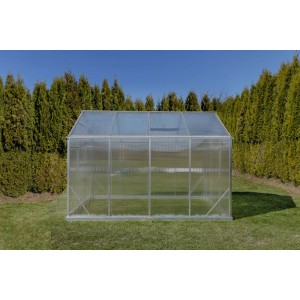 Przezroczysta szklarnia t.b.t. w ogrodzie, otoczona zielonymi drzewami.