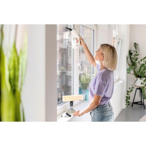 Kobieta czyści okno za pomocą akumulatorowej myjki do okien. Widoczne akcesoria.