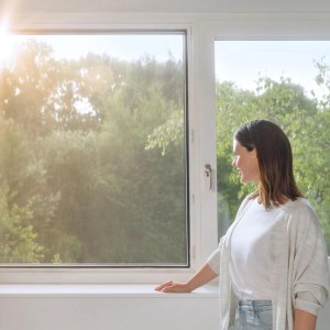 Kobieta przy oknie z siatką pyłkową Tesa antracyt. Skuteczna ochrona przed pyłkami.