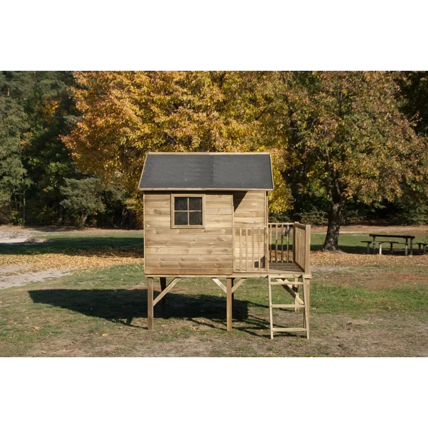 Drewniany domek do zabawy t.b.t. na palach z drabinką i małym balkonem na tle jesieni.
