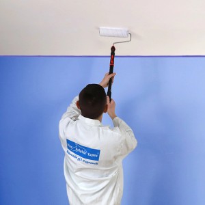Mężczyzna maluje sufit wałkiem. Teleskopowy wałek do malowania sufitów.