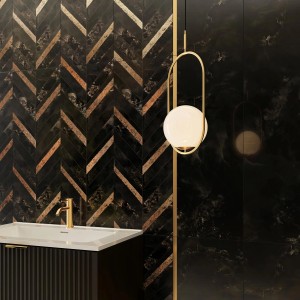 Dekoracyjna ściana z ciemnych płytek i wzorem w jodełkę, połączona ze złotą lampą.