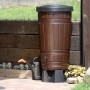 Brązowa beczka na deszczówkę Waterform Woodcan 265 l z efektem drewna i konewką w ogrodzie.