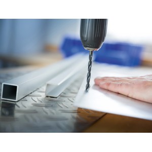 Wiertło do metalu LUX wierci w metalowej płycie, obrabiane elementy w tle.