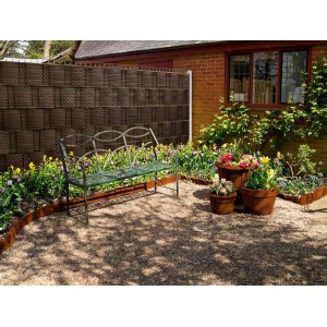 Brązowa mata jako ogrodzenie z ławką i rabatami kwiatowymi.