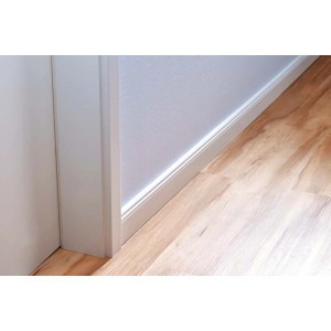 Zbliżenie białej listwy przypodłogowej i ramy drzwi na tle drewnianej podłogi i białej ściany.