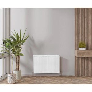 Biały grzejnik t.b.t. na tle szarej ściany w pokoju.