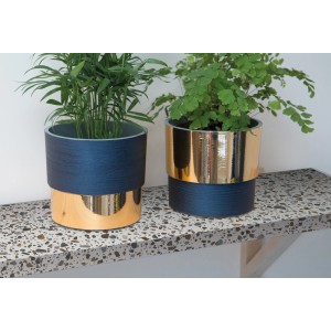 Dwie niebieskie doniczki ze złotym obramowaniem i roślinami na wzorzystej powierzchni.