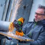 Mężczyzna szlifuje metal akumulatorową szlifierką kątową LUX A-WS-20/115. Lecą iskry.