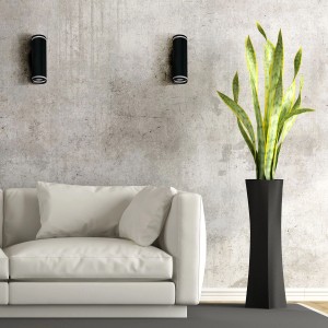 Dwa czarne kinkiety na szarej ścianie nad białą sofą i rośliną.