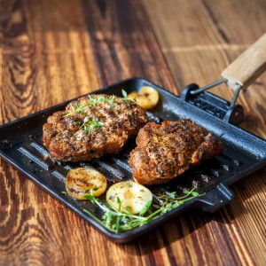 Grillowane mięso z cebulą i ziołami na czarnej patelni grillowej.