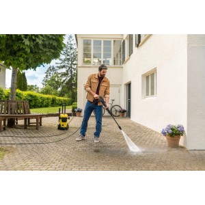 Mężczyzna czyści kostkę brukową przed domem za pomocą żółtej myjki ciśnieniowej.