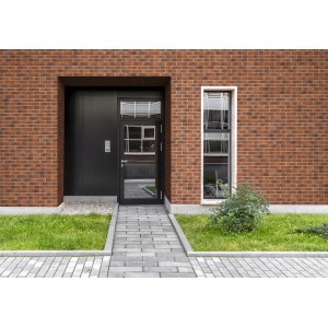 Fasada domu z cegłami klinkierowymi t.b.t. w kolorze czerwono-brązowym i ciemnymi drzwiami.