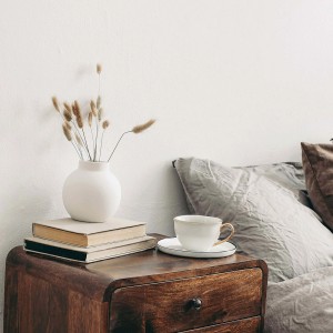 Stolik nocny z dekoracją: wazon, książki i filiżanka. Farba na ścianę może być kolorowa.