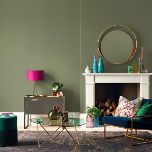 Salon z oliwkowozieloną farbą na ścianach, kominkiem i kolorowymi elementami dekoracyjnymi.
