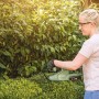Kobieta przycina żywopłot akumulatorowymi nożycami do żywopłotu. t.b.t.