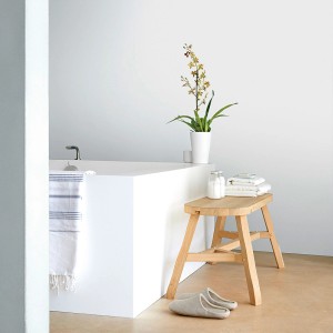 Scena łazienki z wanną, stołkiem, rośliną i ręcznikami w jasnych kolorach.